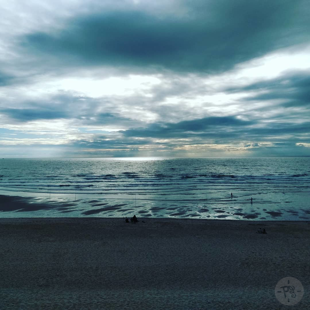 Photographie prise par Pauline pour Positiv'évidence, représentant une plage avec l'écume des vagues ainsi que l'horizon et le ciel bleu-gris car nuageux. Au milieu de la photographie est écrit : "Créer la paix en soi-même et tout autour".